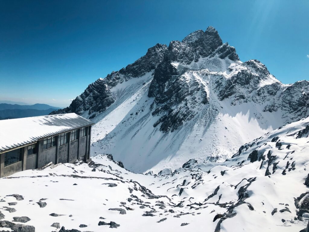 pexels-photo-10836116-10836116 Breathtaking winter scene of Yulong Snow Mountain in Lijiang, China with a rustic cabin.