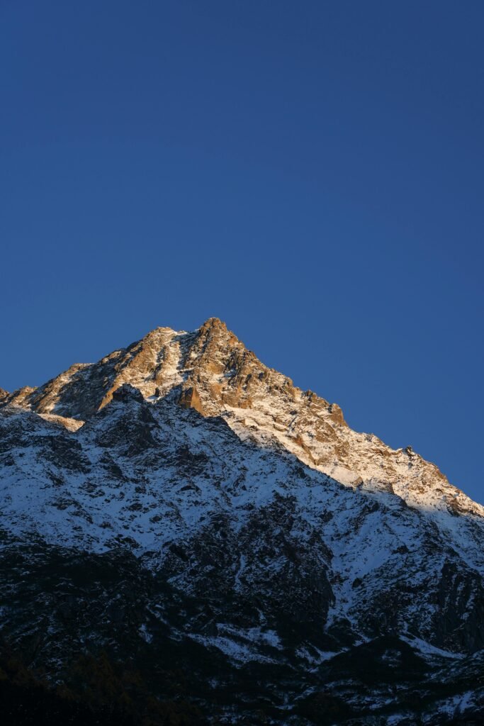 pexels-photo-34613802-34613802 Snowy mountain peak glistens under a clear blue sky at sunset, capturing nature's beauty.